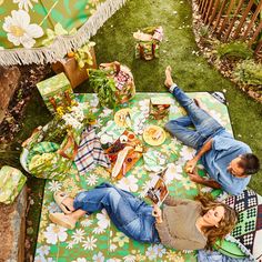 two people laying on a green and white flowered picnic blanket in the grass with food