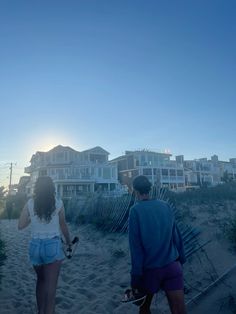 two people are walking on the beach near some houses