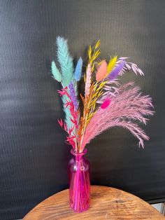 a pink vase filled with colorful flowers on top of a wooden table next to a black wall