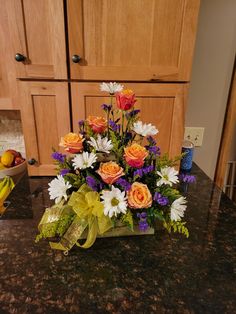 a bouquet of flowers sitting on top of a counter next to a bowl of fruit