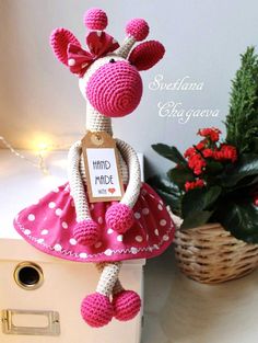 a knitted giraffe doll sitting on top of a box next to a potted plant