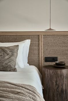 a bed with white sheets and pillows next to a night stand on a wooden table