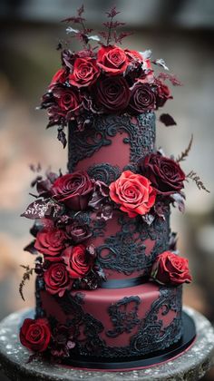 a red and black wedding cake with roses on it's tiered layer, sitting on top of a stone slab