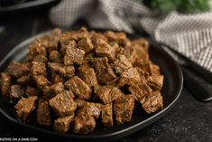 a black plate filled with cubed meat on top of a table next to silverware