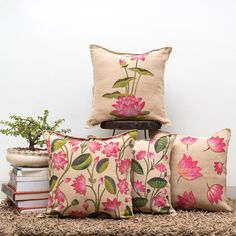 three pillows with pink flowers on them sitting next to books and a potted plant