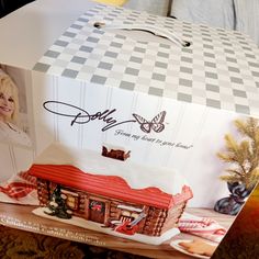 a box that has a house inside of it with the lid open and an image of dolly on top