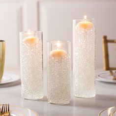 three tall glass vases filled with water and lit candles on a dining room table