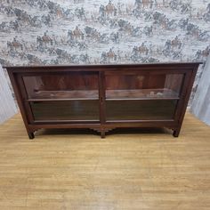 a wooden cabinet sitting on top of a hard wood floor next to a wallpapered wall