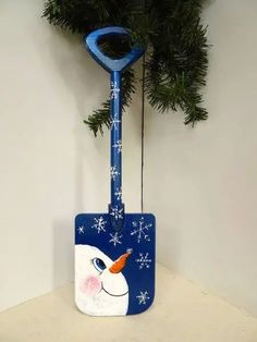 a snowman's head is attached to a blue shovel holder with pine branches in the background