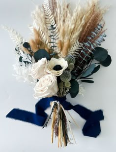 an arrangement of flowers and feathers on a white background with blue ribbon tied around it