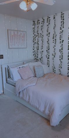 a white bed sitting in a bedroom next to a wall with vines on the walls