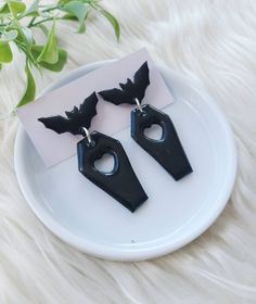 two black earrings on a white plate next to a plant