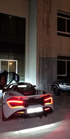 a white sports car parked in front of a building with its doors open at night