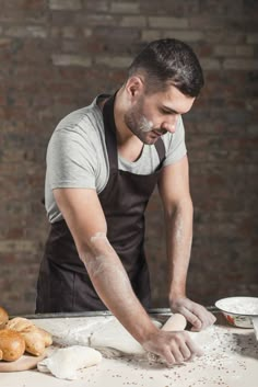 a man in an apron is kneading dough on a table with croissants