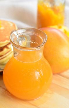 an orange juice in a glass pitcher next to some pancakes