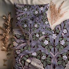 an image of a bed with flowers and leaves on the comforter cover, next to a plant