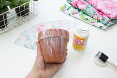 a person is holding a clay pot on a table next to some crafting supplies