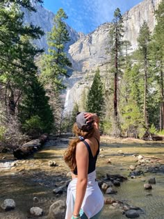 a woman is standing in the middle of a river and looking up into the sky