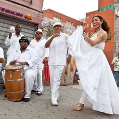 a group of people standing around each other in front of a building with a woman holding a white dress