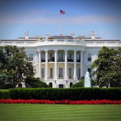 the white house in washington d c, with red flowers and trees around it's perimeter