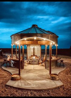 an outdoor gazebo with lights on the sides and chairs around it at night time