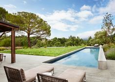 an outdoor swimming pool with lounge chairs and tables next to it, surrounded by greenery