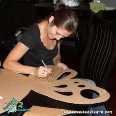 a woman sitting at a table making a paper cutout