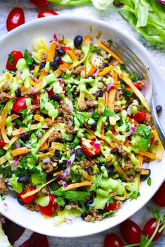 a salad with lettuce, tomatoes, black olives and ground beef in a white bowl