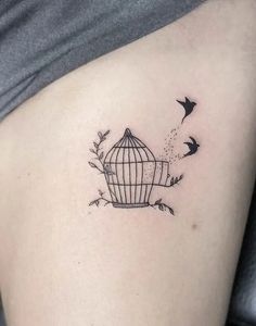 a small birdcage tattoo on the side of a woman's stomach with birds flying around it