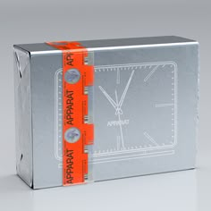 a silver box with an orange ribbon around the edges and a clock on it's side