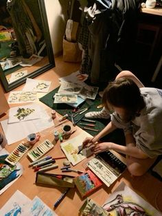 a young boy sitting on the floor working on some art work in front of a mirror