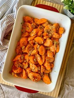 a casserole dish filled with cooked carrots on a wooden cutting board next to a potted plant