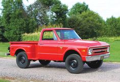 an old red pickup truck parked on the side of a road in front of some trees