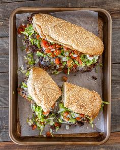 two sandwiches with lettuce, tomato and other toppings on a baking sheet