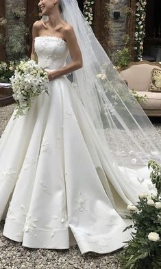 a woman in a white wedding dress standing next to a flowered arch with flowers on it