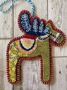 an ornament shaped like a horse on a wooden floor with blue and yellow thread