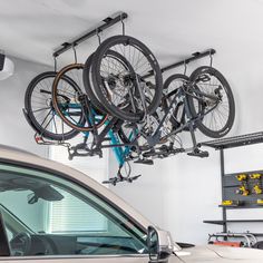 two bikes are hanging from the ceiling in a garage with cars parked underneath and tools on the wall