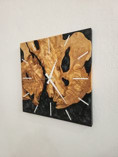 a wooden clock mounted to the side of a white wall next to a black and gold painting