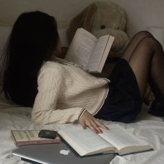 a woman laying in bed reading a book and holding a teddy bear next to her