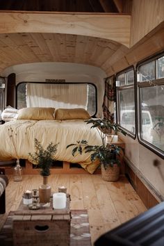 the interior of a camper with wood flooring and walls, windows, and bed