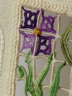 an embroidered piece with flowers on it is shown in purple and green colors, as well as white thread