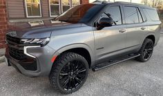 a silver suv parked in front of a brick building with black wheels and rims