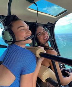 two women are sitting in the cockpit of an airplane with headset's on