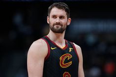 a man with a beard wearing a black and red uniform standing in front of a basketball court