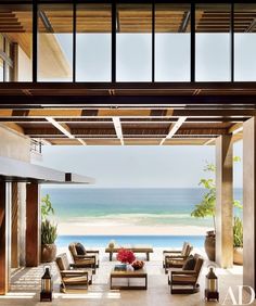 an outdoor living area with chairs and tables next to the beach in front of it