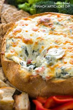 bread bowl spinach artichoke dip with broccoli and carrots in the background