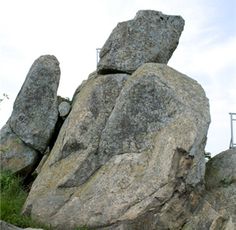 a man standing on top of a large rock next to a green grass covered field