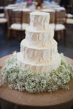 a white wedding cake with baby's breath on top and greenery around it