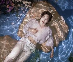 a woman laying on top of a body of water next to plants and flowers in the water