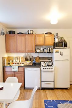 a small kitchen with white appliances and wooden cabinets, along with a dining room table